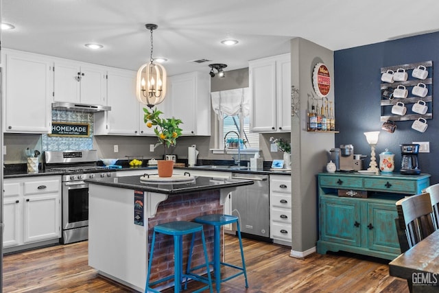 kitchen with white cabinets, appliances with stainless steel finishes, a center island, a kitchen bar, and sink