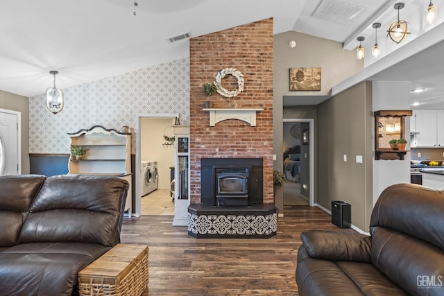 living room with hardwood / wood-style flooring, a wood stove, lofted ceiling, and washing machine and dryer