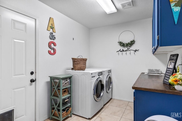 clothes washing area with a textured ceiling, cabinets, light tile patterned floors, and washer and clothes dryer