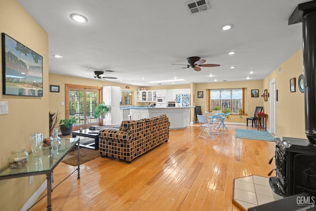 living room with ceiling fan, recessed lighting, visible vents, light wood finished floors, and a wood stove