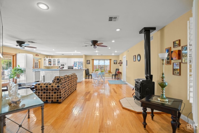 living area with recessed lighting, visible vents, a ceiling fan, light wood-style floors, and a wood stove