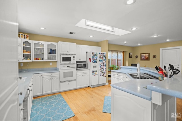 kitchen featuring glass insert cabinets, white appliances, a skylight, and white cabinets