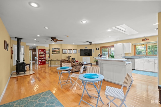 interior space featuring a center island, a wood stove, light wood-style floors, white cabinetry, and stainless steel dishwasher