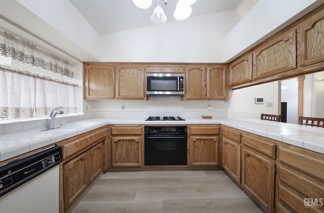 kitchen featuring tile countertops, black appliances, sink, light hardwood / wood-style flooring, and a chandelier