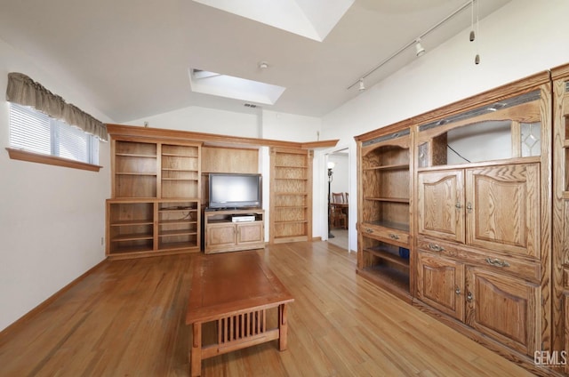 unfurnished living room featuring lofted ceiling with skylight, rail lighting, and light hardwood / wood-style floors