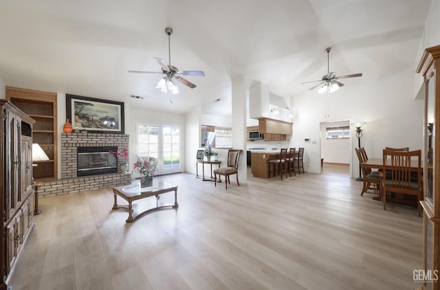 living room with ceiling fan, a fireplace, vaulted ceiling, and light wood-type flooring