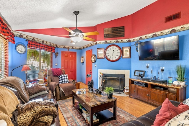 living room featuring lofted ceiling, wood-type flooring, a textured ceiling, ceiling fan, and a tiled fireplace