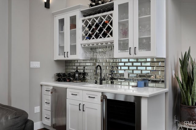 bar featuring white cabinets, sink, beverage cooler, and backsplash