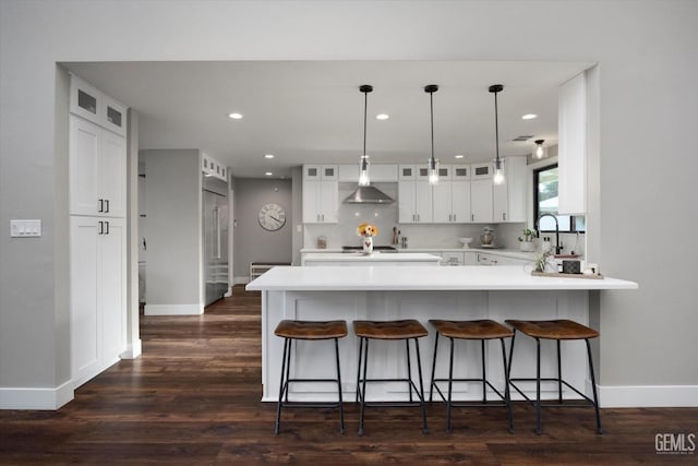 kitchen featuring decorative light fixtures, white cabinets, dark hardwood / wood-style flooring, kitchen peninsula, and wall chimney exhaust hood