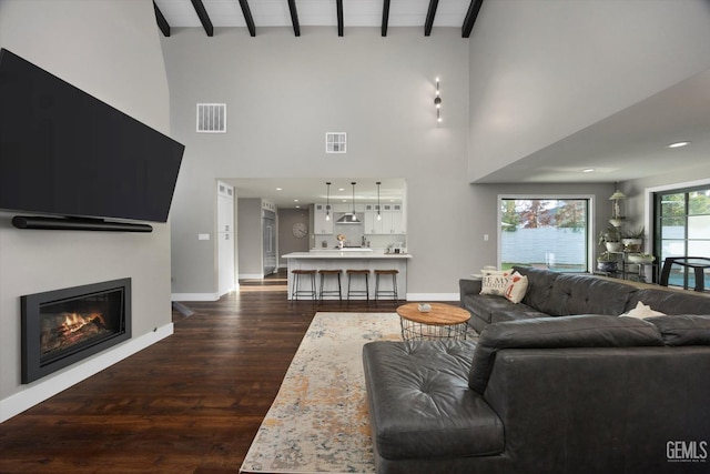 living room with a towering ceiling, dark hardwood / wood-style floors, and beam ceiling