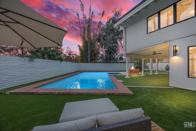 pool at dusk featuring ceiling fan, a yard, and outdoor lounge area