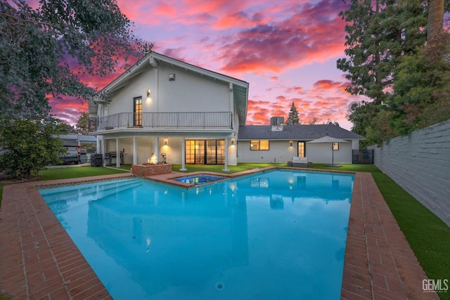 pool at dusk featuring an in ground hot tub and a yard