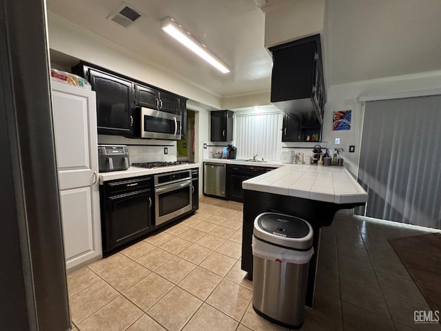 6301 Scenic Way, Bakersfield, CA 93309 - kitchen featuring appliances with stainless steel finishes, dark cabinets, tile counters, light tile patterned floors, and ornamental molding