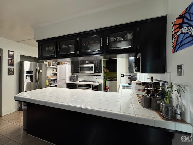 6301 Scenic Way, Bakersfield, CA 93309 - kitchen featuring dark cabinetry, crown molding, stainless steel appliances, glass insert cabinets, and tile countertops