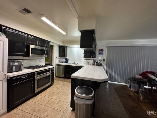6301 Scenic Way, Bakersfield, CA 93309 - kitchen with dark cabinetry, appliances with stainless steel finishes, tile counters, light tile patterned floors, and ornamental molding