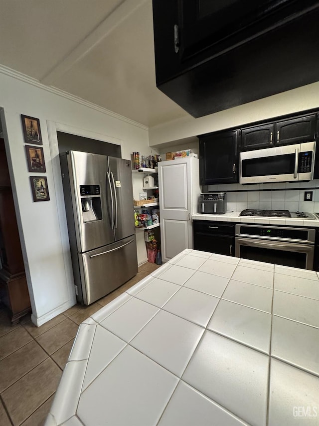 6301 Scenic Way, Bakersfield, CA 93309 - kitchen with dark cabinetry, appliances with stainless steel finishes, ornamental molding, tile countertops, and tile patterned flooring