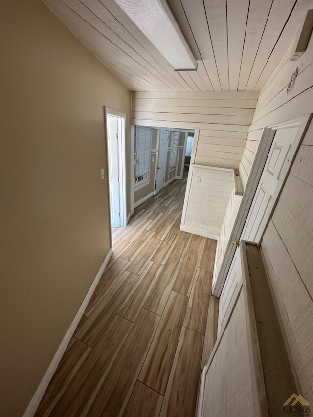 corridor featuring wood tiled floor, lofted ceiling, and baseboards