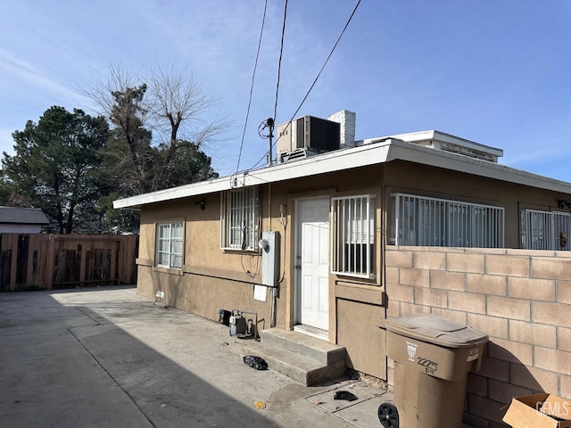 view of side of home with cooling unit, fence, and stucco siding