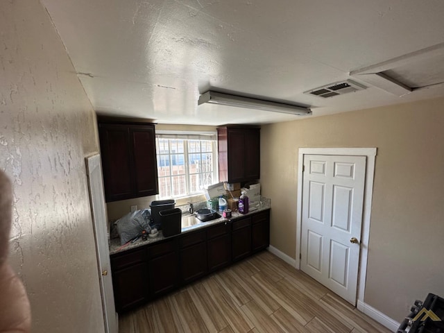 kitchen with baseboards, visible vents, dark brown cabinets, light wood-type flooring, and a sink