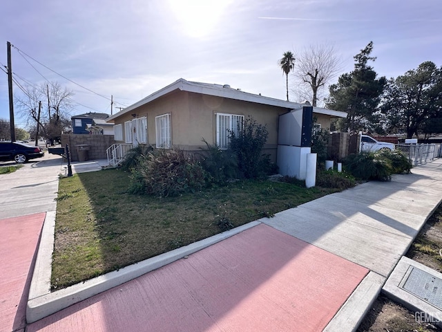 view of property exterior with fence, a lawn, and stucco siding