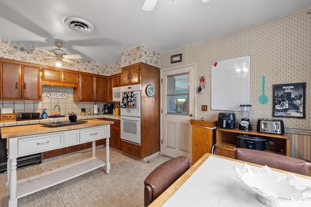 kitchen featuring double oven, visible vents, ceiling fan, and wallpapered walls