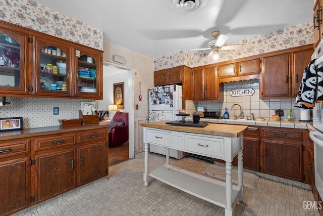 kitchen with visible vents, a ceiling fan, glass insert cabinets, a sink, and wallpapered walls