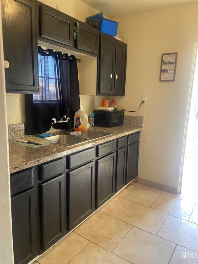 kitchen with light tile patterned floors, stone countertops, and sink