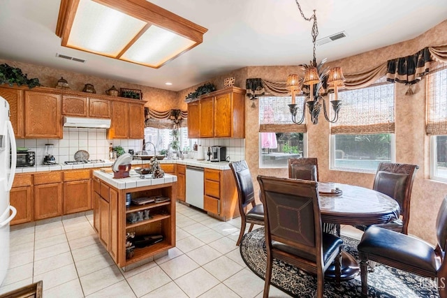 kitchen featuring an inviting chandelier, tile counters, under cabinet range hood, brown cabinetry, and white appliances