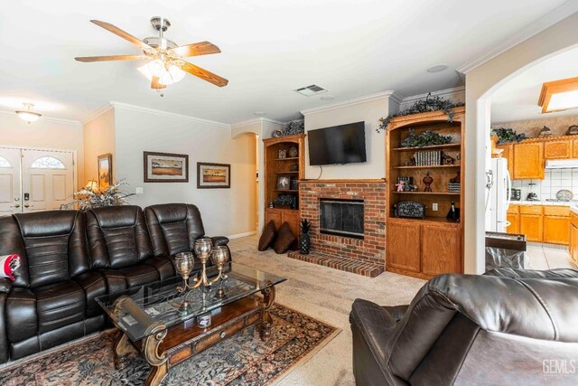 living area featuring a fireplace, a ceiling fan, visible vents, ornamental molding, and arched walkways