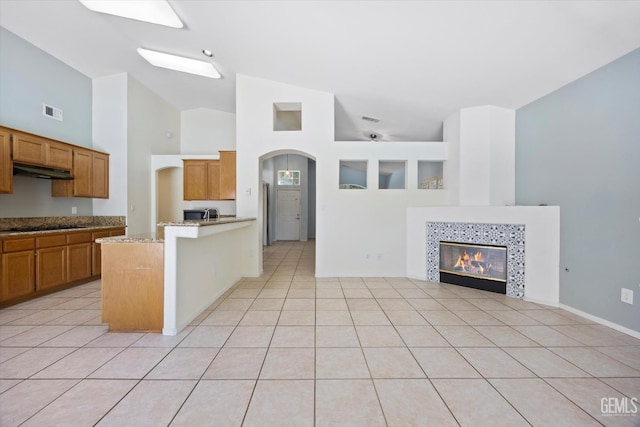 5836 S Greenhorn Mountain Ct, Bakersfield, CA 93313 - kitchen with under cabinet range hood, a tiled fireplace, light tile patterned flooring, a peninsula, and open floor plan