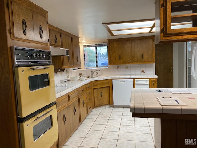 kitchen with sink, dishwasher, multiple ovens, tile countertops, and light tile patterned floors