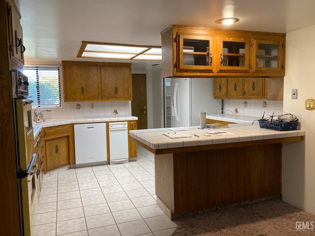 kitchen with white appliances, backsplash, light tile patterned floors, tile counters, and kitchen peninsula