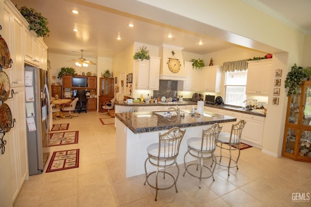 kitchen with dark stone countertops, a breakfast bar area, an island with sink, and stainless steel refrigerator with ice dispenser