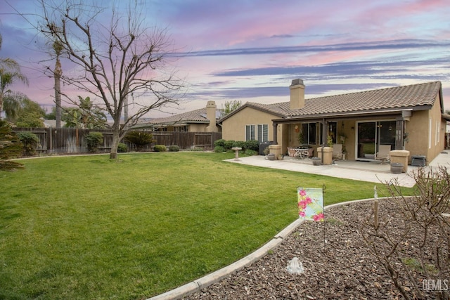 back house at dusk featuring a patio area and a lawn