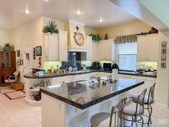 kitchen featuring a breakfast bar, light tile patterned floors, white gas stovetop, a kitchen island with sink, and white cabinets