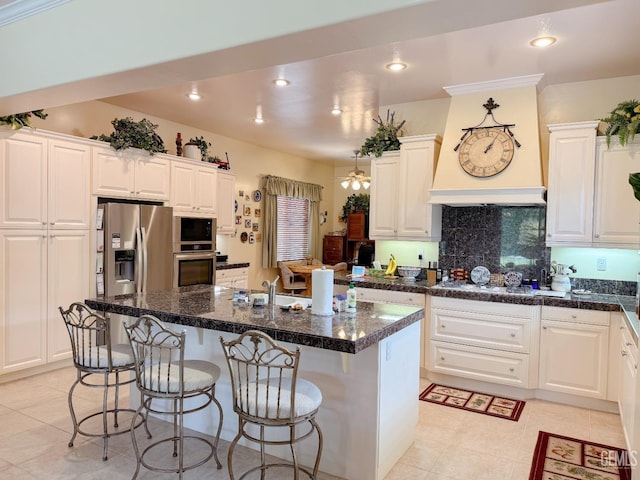 kitchen with white cabinetry, appliances with stainless steel finishes, a kitchen island with sink, and dark stone counters