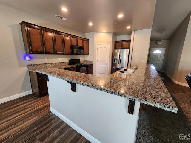 1756 Bautista Ave, Wasco, CA 93280 - kitchen with black appliances, dark wood-style flooring, a breakfast bar area, dark brown cabinetry, and recessed lighting