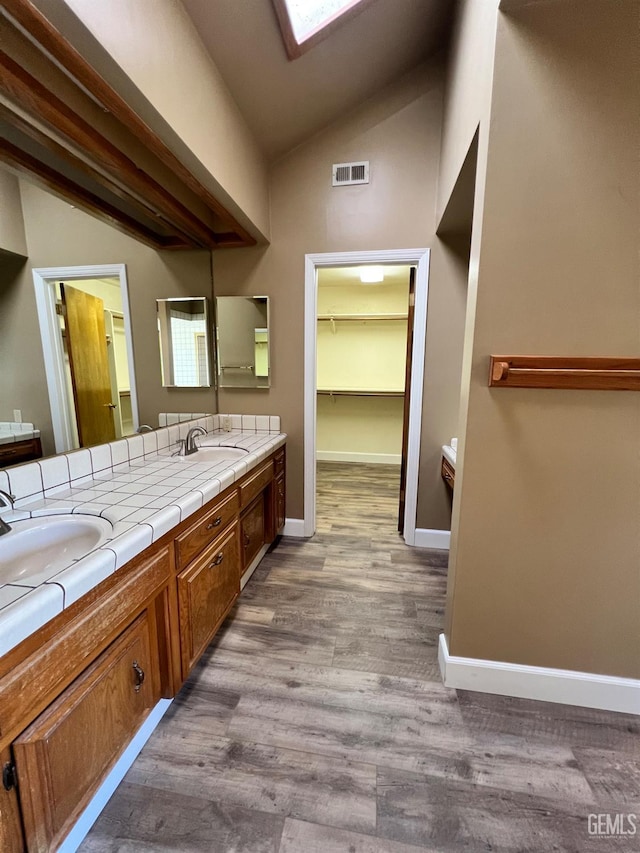 5306 Deville Ct, Bakersfield, CA 93308 - bathroom with vaulted ceiling, a skylight, double vanity, and wood finished floors