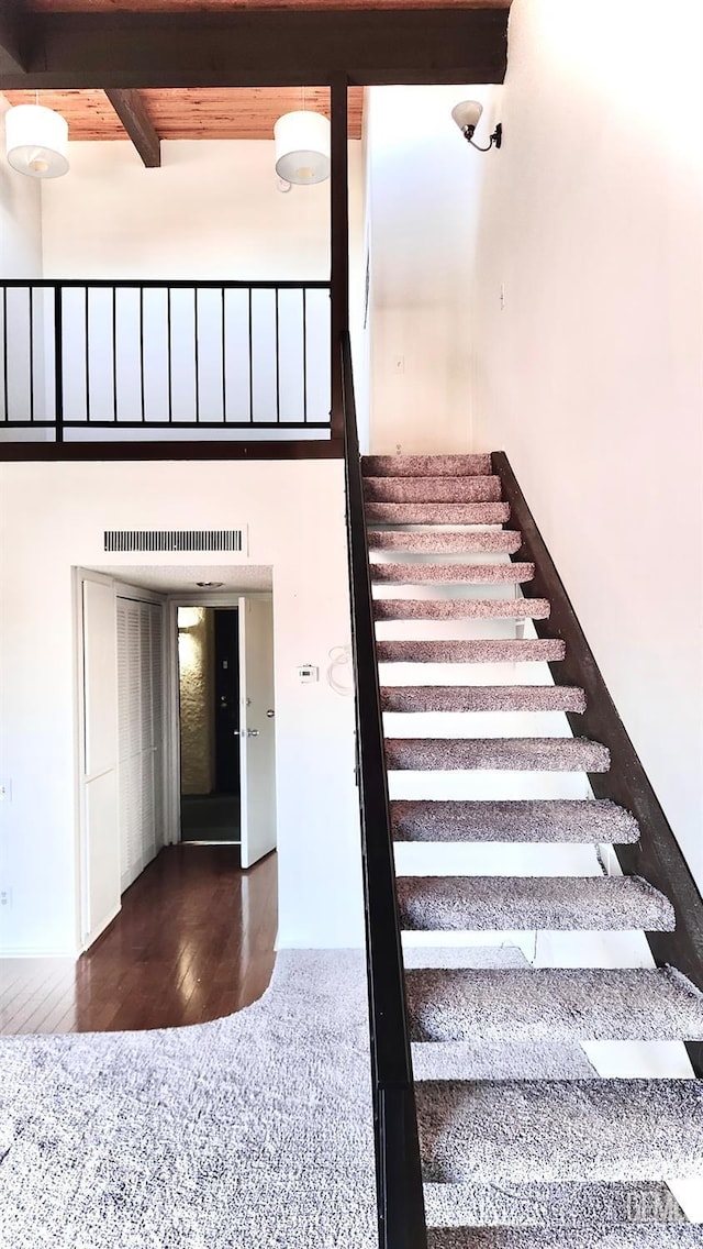 stairs featuring a towering ceiling, hardwood / wood-style floors, beamed ceiling, and wooden ceiling