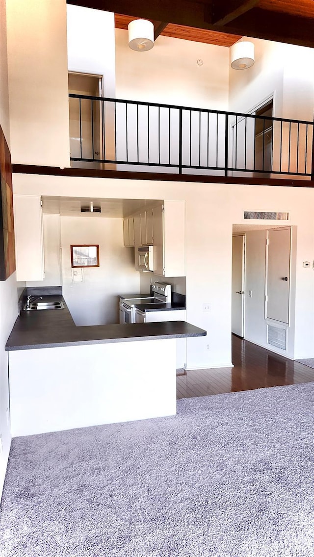 kitchen with stainless steel range with electric stovetop, kitchen peninsula, sink, a towering ceiling, and white cabinetry