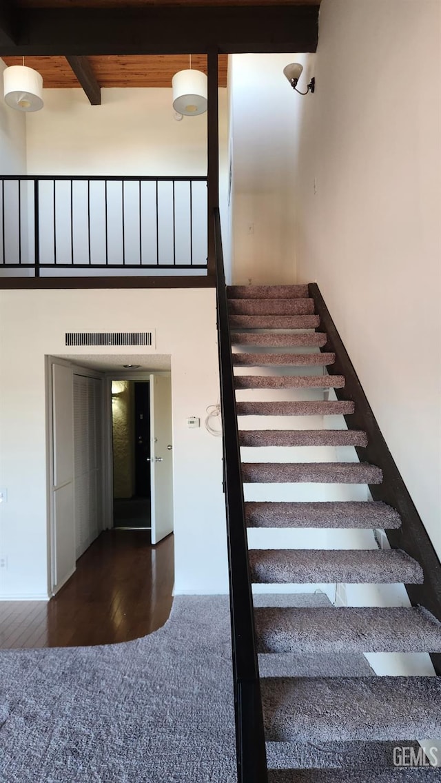 stairway featuring beam ceiling, a towering ceiling, wood ceiling, and hardwood / wood-style floors