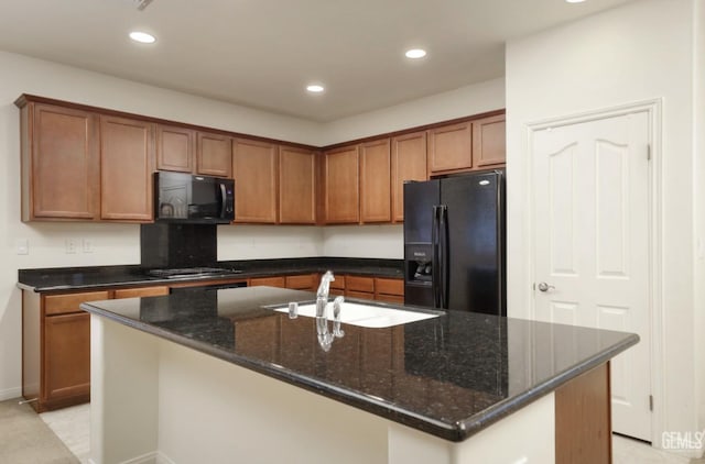 kitchen featuring black appliances, dark stone countertops, sink, and an island with sink