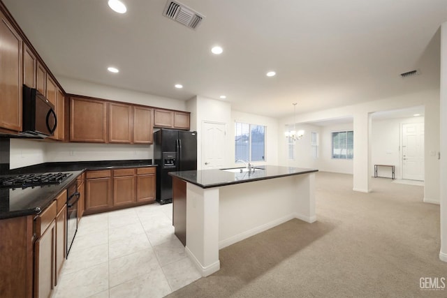 kitchen featuring a notable chandelier, light carpet, a kitchen island with sink, black appliances, and decorative light fixtures