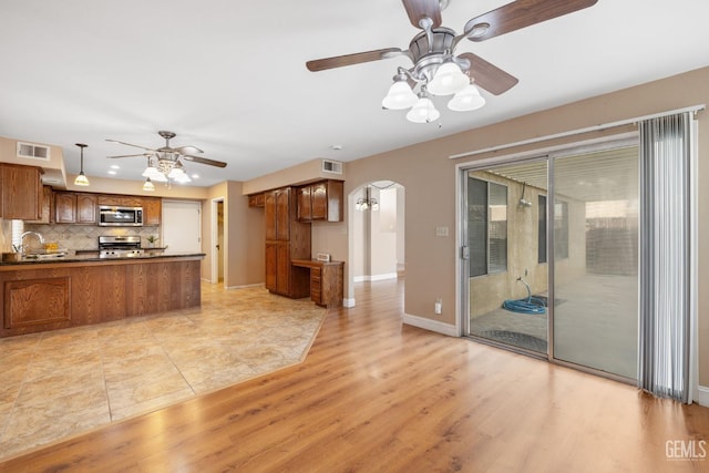 kitchen featuring backsplash, ceiling fan, kitchen peninsula, stainless steel appliances, and light hardwood / wood-style flooring