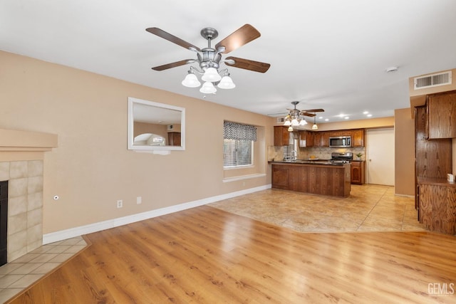 kitchen with light hardwood / wood-style flooring, a tile fireplace, backsplash, stainless steel appliances, and kitchen peninsula