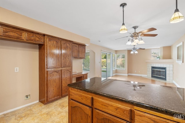 kitchen featuring a tiled fireplace, decorative light fixtures, dark stone countertops, and ceiling fan