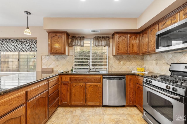 kitchen featuring appliances with stainless steel finishes, pendant lighting, sink, dark stone countertops, and backsplash