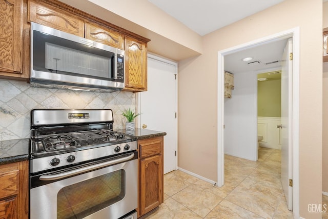 kitchen with stainless steel appliances, tasteful backsplash, light tile patterned flooring, and dark stone counters