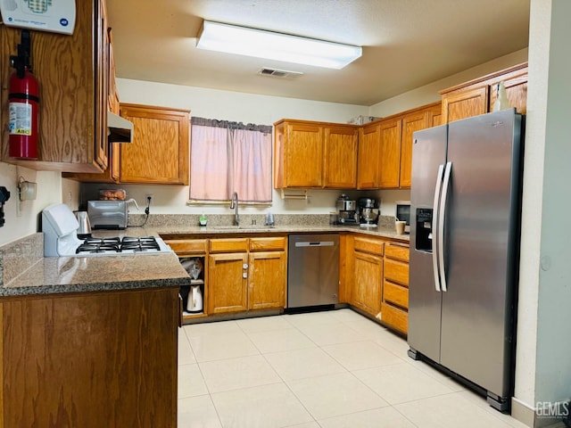 kitchen with light tile patterned floors, stainless steel appliances, dark stone counters, and sink