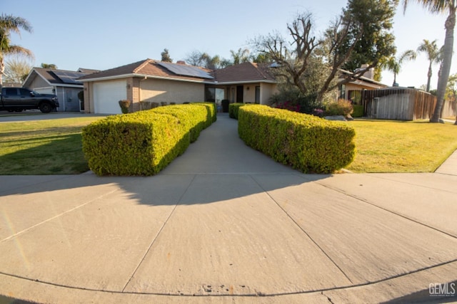 ranch-style home with driveway, roof mounted solar panels, an attached garage, and a front lawn